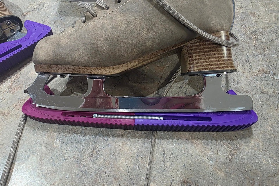 A figure skating blade mounted on a tan boot, seen from the side, with a purple guard over the edge