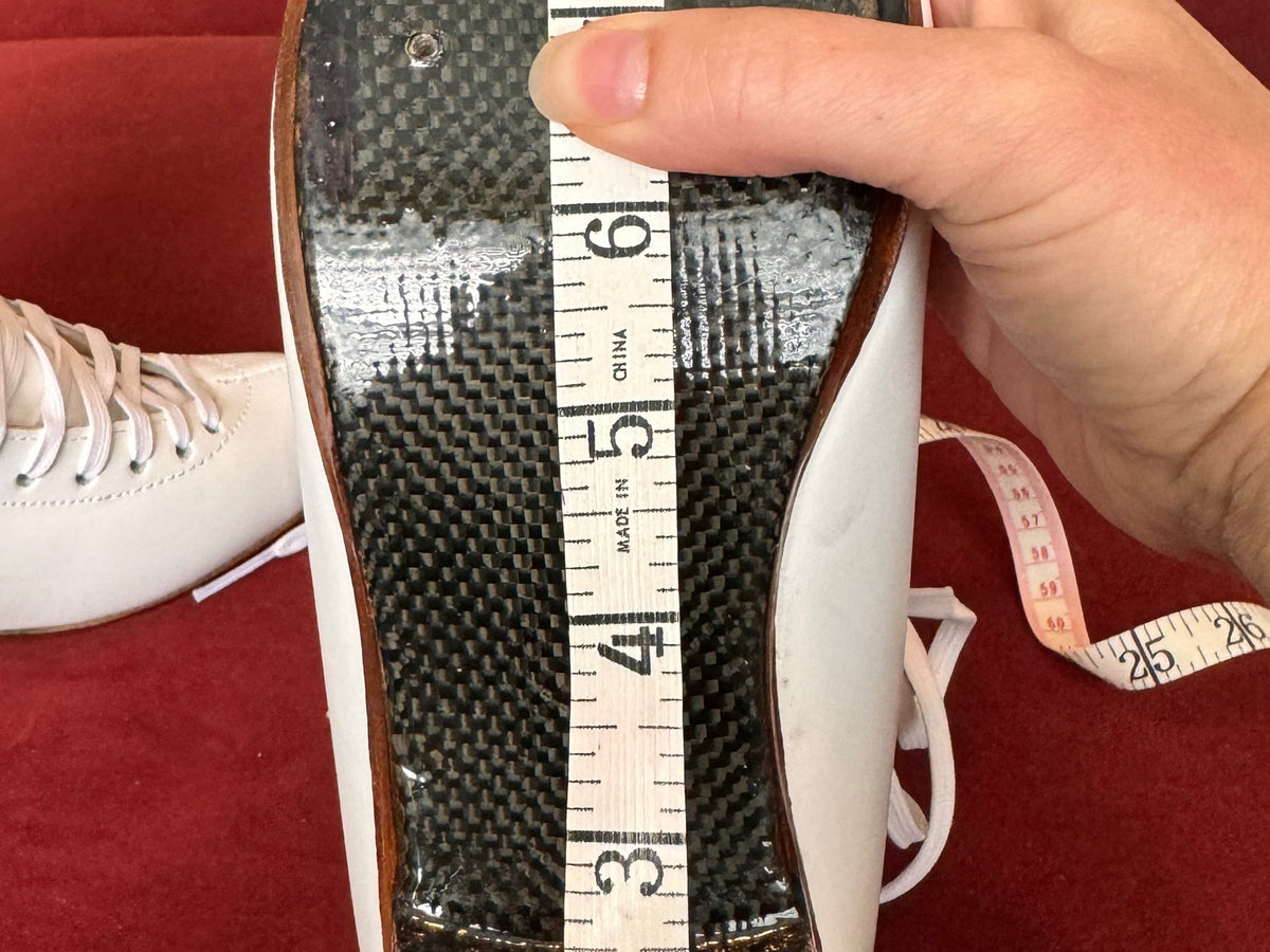 A tape measure held along the sole of a white figure skating boot