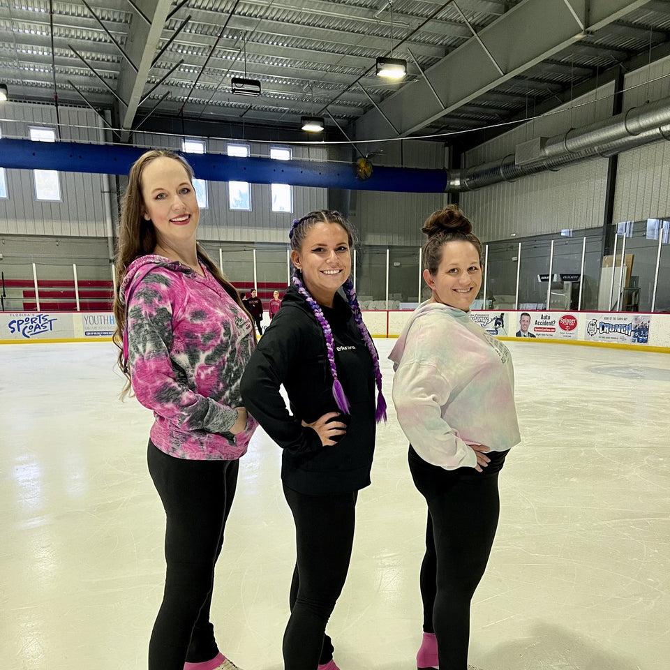 Three adult skaters in hoodies standing together on the ice