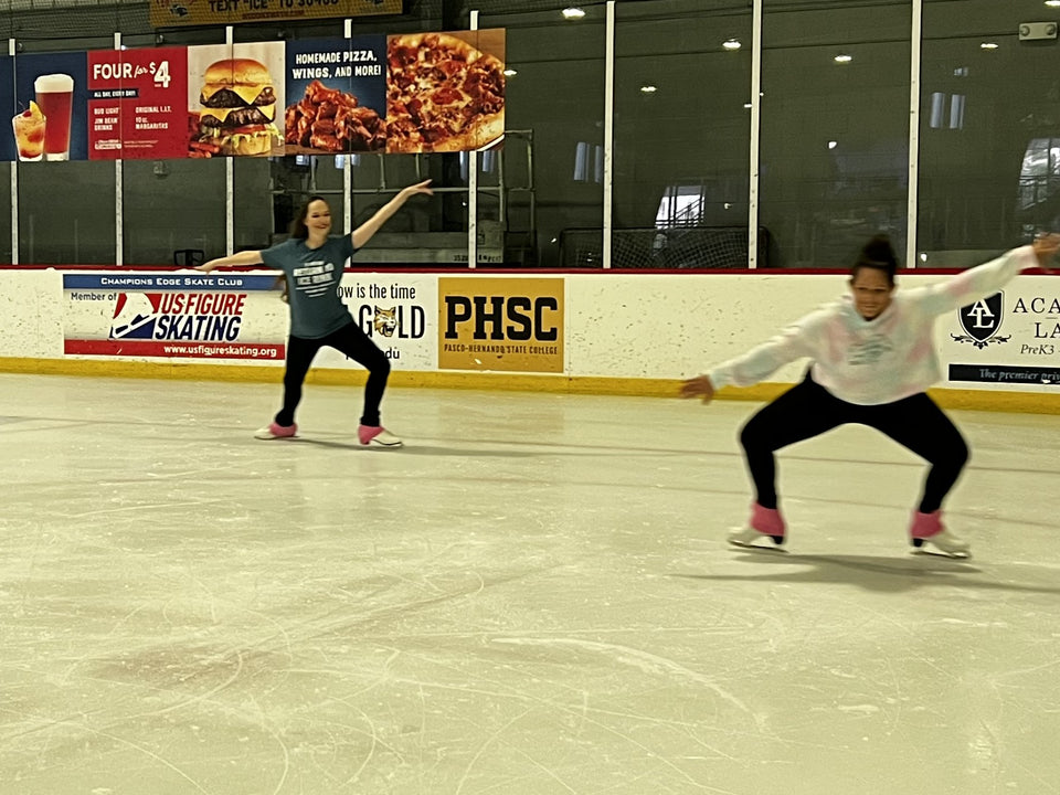 Two adult skaters practising on a quiet rink, one in a deep knee bend