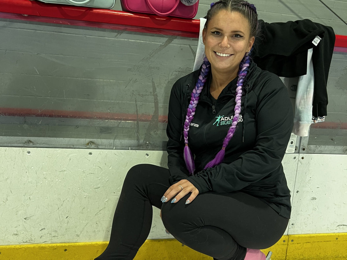 An adult skater sitting on the rink boards in a black jacket
