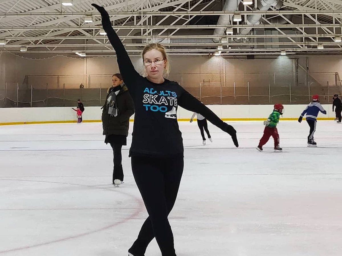 An adult skater in an Adults Skate Too top posing with her arms out on the ice