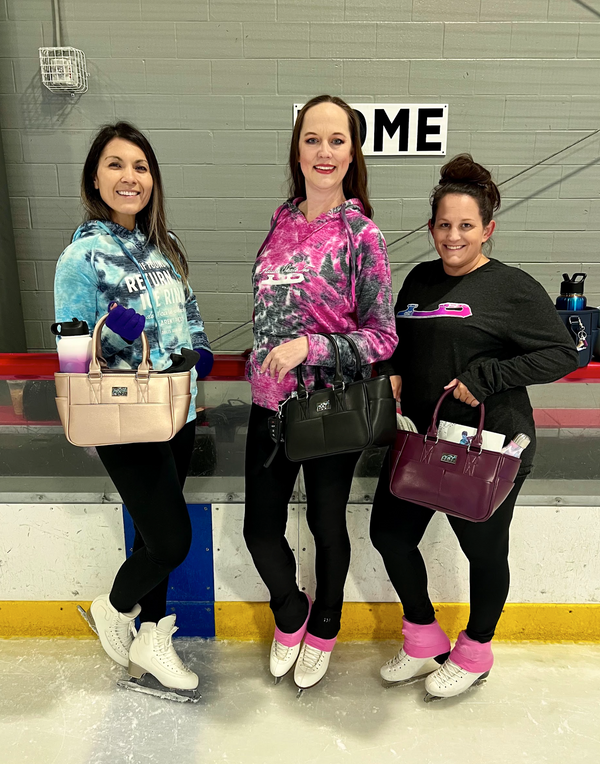 Three skaters in tie-dye and black tops holding Adults Skate Too totes by the rink.
